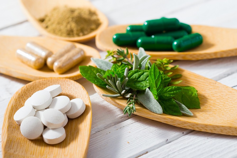Capsules and herbs on wooden spoons