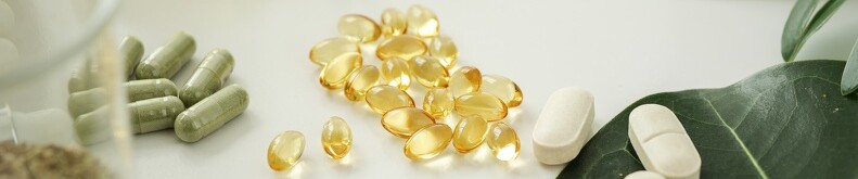 Different capsules and pills on a table with some leaves